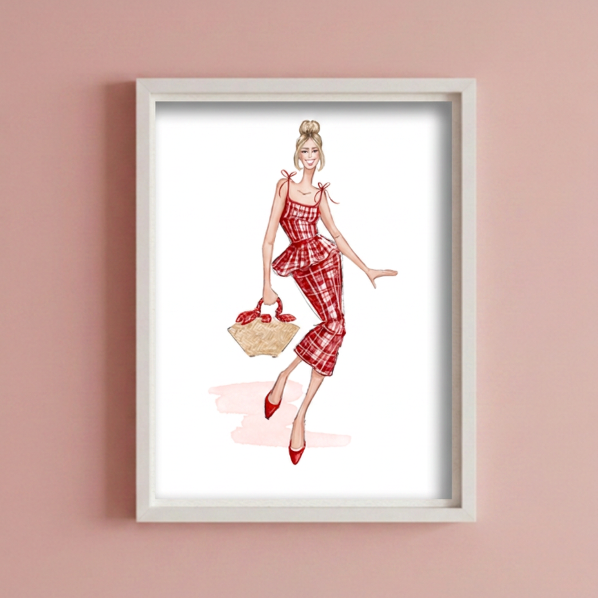 A framed fashion illustration print of a woman in a red and white plaid dress and  holding a handbag, displayed on a dusty pink wall.